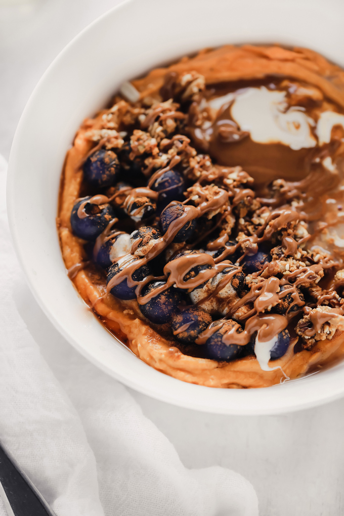 Vegan Sweet Potato Breakfast Bowl - Topped with blueberries, almond butter, and dairy free yogurt, this is packed with fiber, healthy fats and so easy to make! You can meal prep this and have it ready to go with all the right ingredients to fuel your day! NeuroticMommy.com #vegan #breakfast #sweetpotatoes