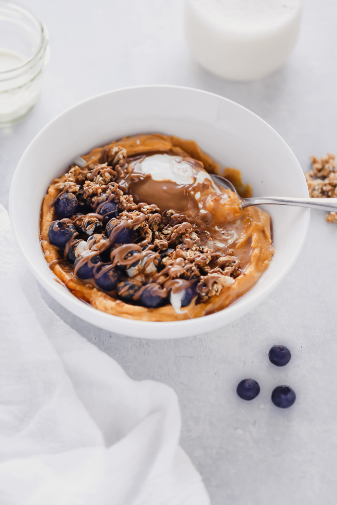 Vegan Sweet Potato Breakfast Bowl - Topped with blueberries, almond butter, and dairy free yogurt, this is packed with fiber, healthy fats and so easy to make! You can meal prep this and have it ready to go with all the right ingredients to fuel your day! NeuroticMommy.com #vegan #breakfast #sweetpotatoes 